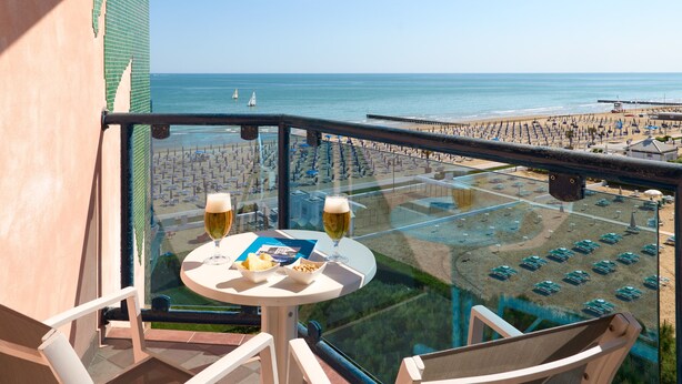 Un balcon avec une table, deux verres de bière et une vue sur la plage et le parking.