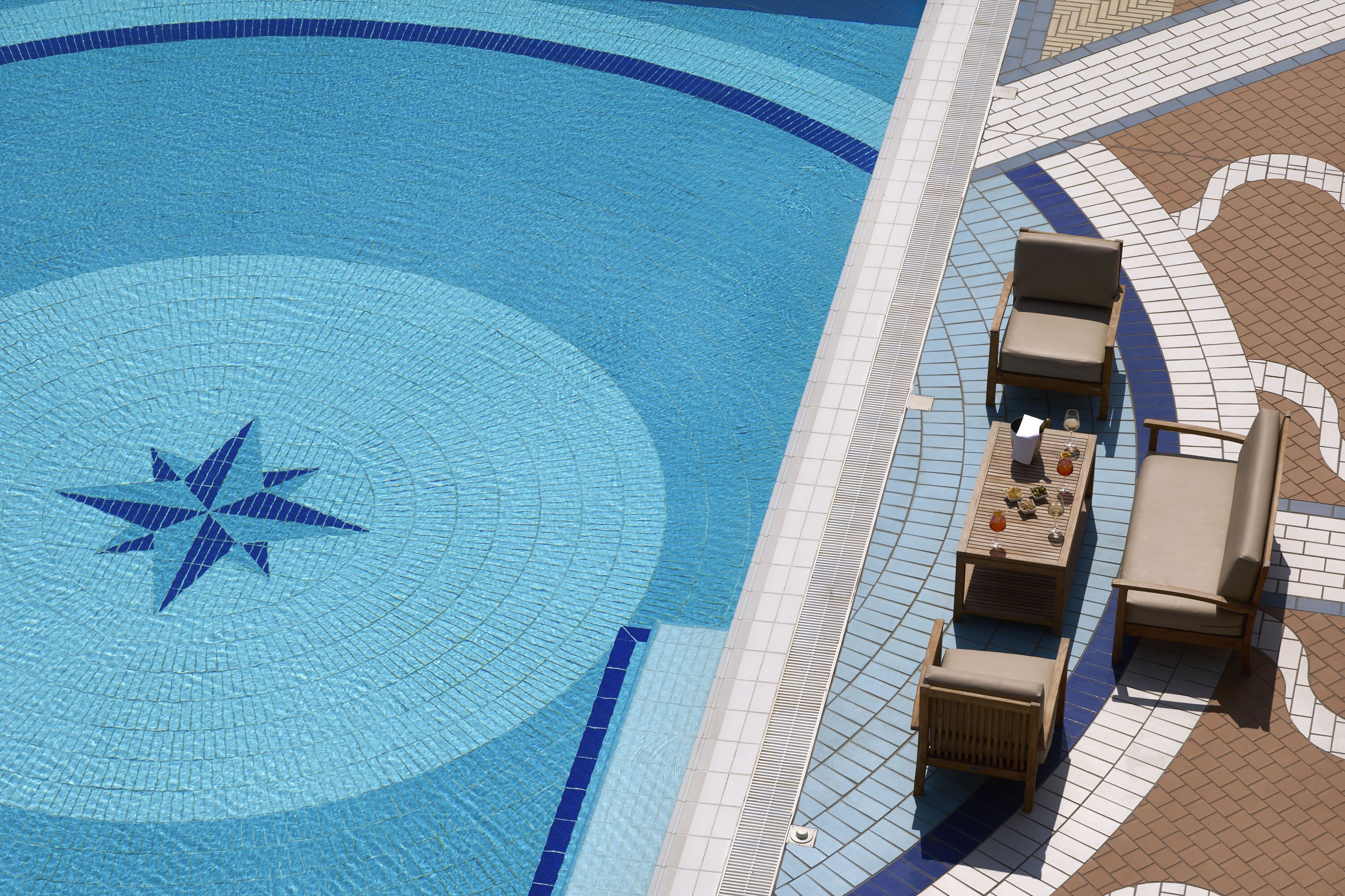 Une piscine en forme d’étoile, entourée d’une terrasse carrelée avec des chaises longues et une table.