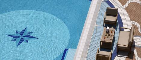 Une piscine en forme d’étoile, entourée d’une terrasse carrelée avec des chaises longues et une table.