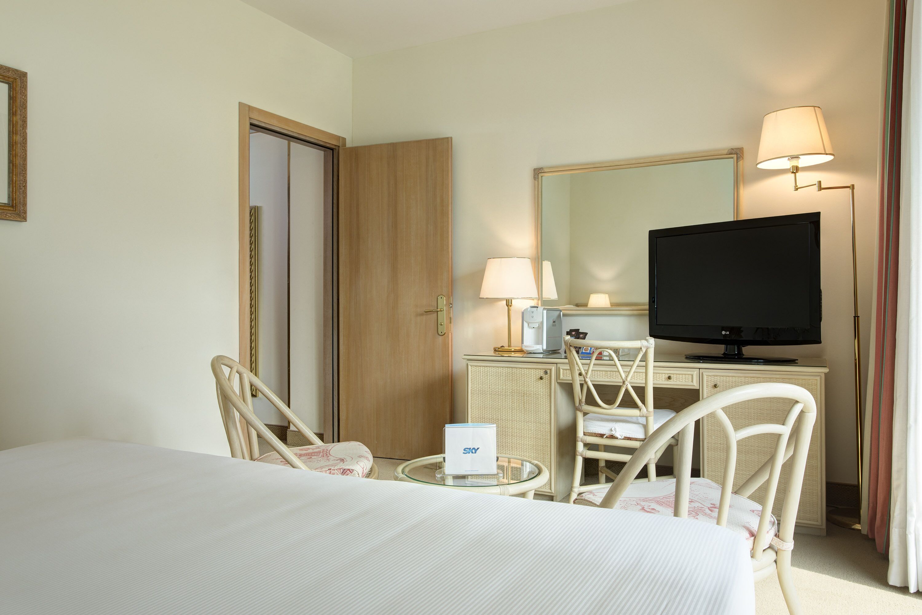 Een hotelkamer met een bed, een bureau met een televisie, een stoel, een lamp en een spiegel.