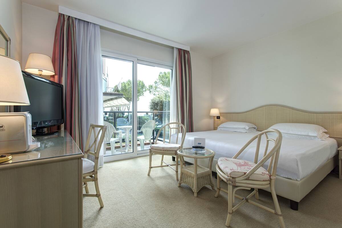 Een hotelkamer met een bed, twee stoelen, een kleine tafel, een televisie en een raam met gordijnen.
