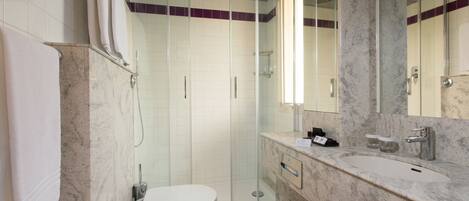 A bathroom with a shower, toilet, sink, and marble walls.