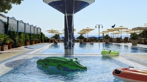 Une piscine agrémentée d’une fontaine centrale, de chaises longues, de parasols et de jeux gonflables.