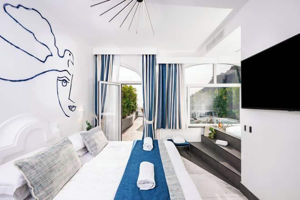 A modern hotel room with a large bed, a blue towel, a TV, and a view of a pool and greenery.