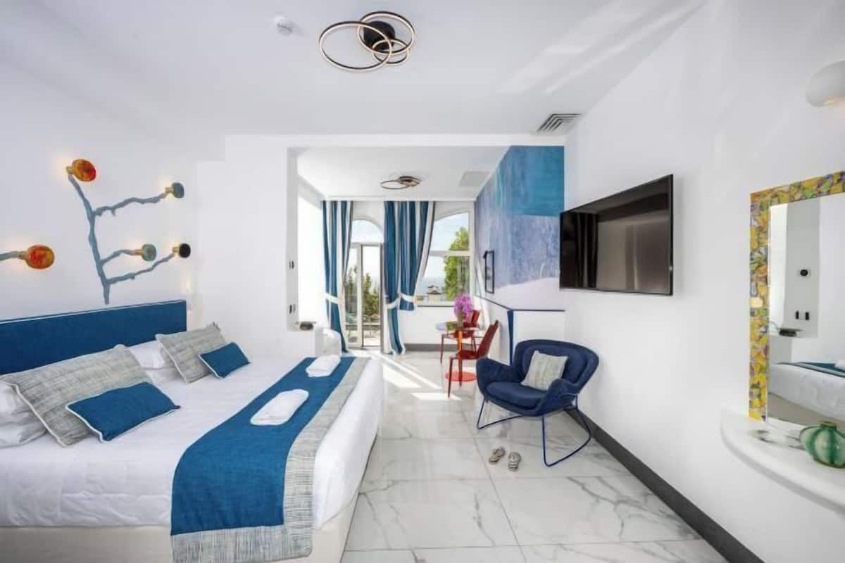 A modern hotel room with a bed, a desk, a chair, a TV, and a bathroom.