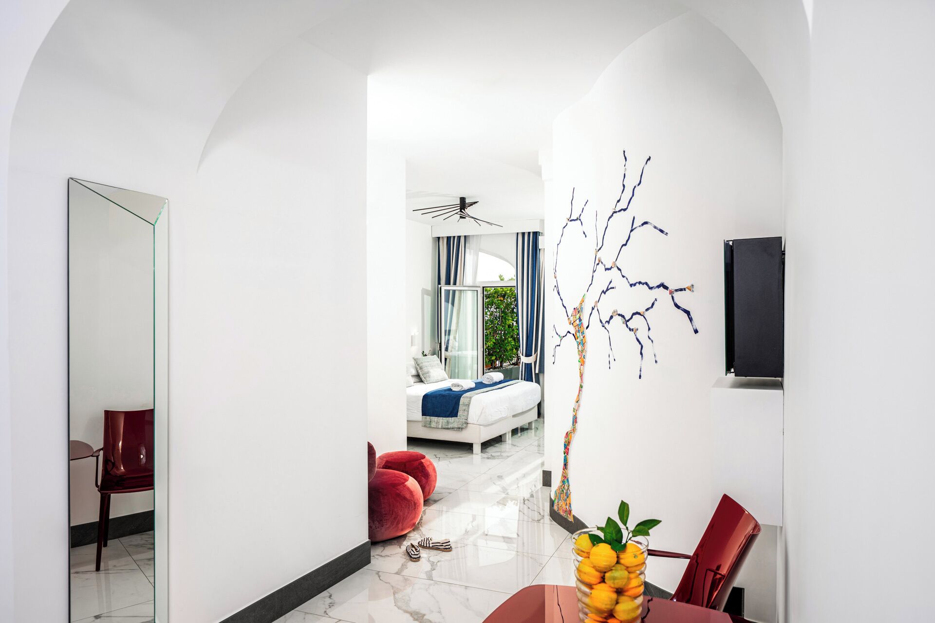 Ein modernes Interieur mit Essbereich, einem roten Sessel, einem Glastisch und Blick in einen weiteren Raum mit Bett und Vorhängen.