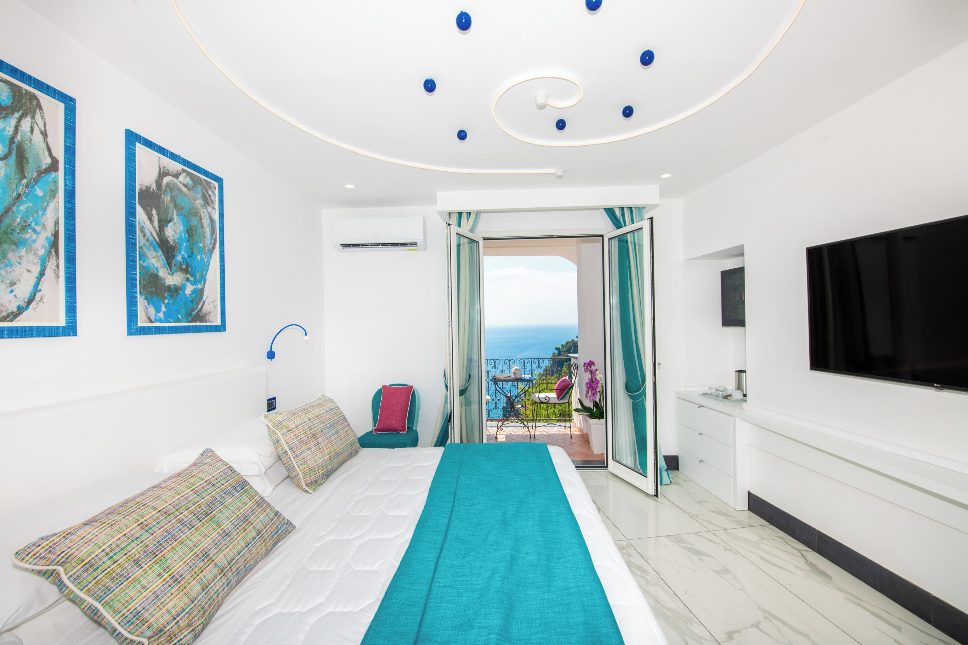 A modern hotel room with a bed, a TV, a balcony with a view, and artwork on the walls.