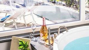 Un baño moderno con un ventanal grande, una bañera y una mesa con una botella y vasos.