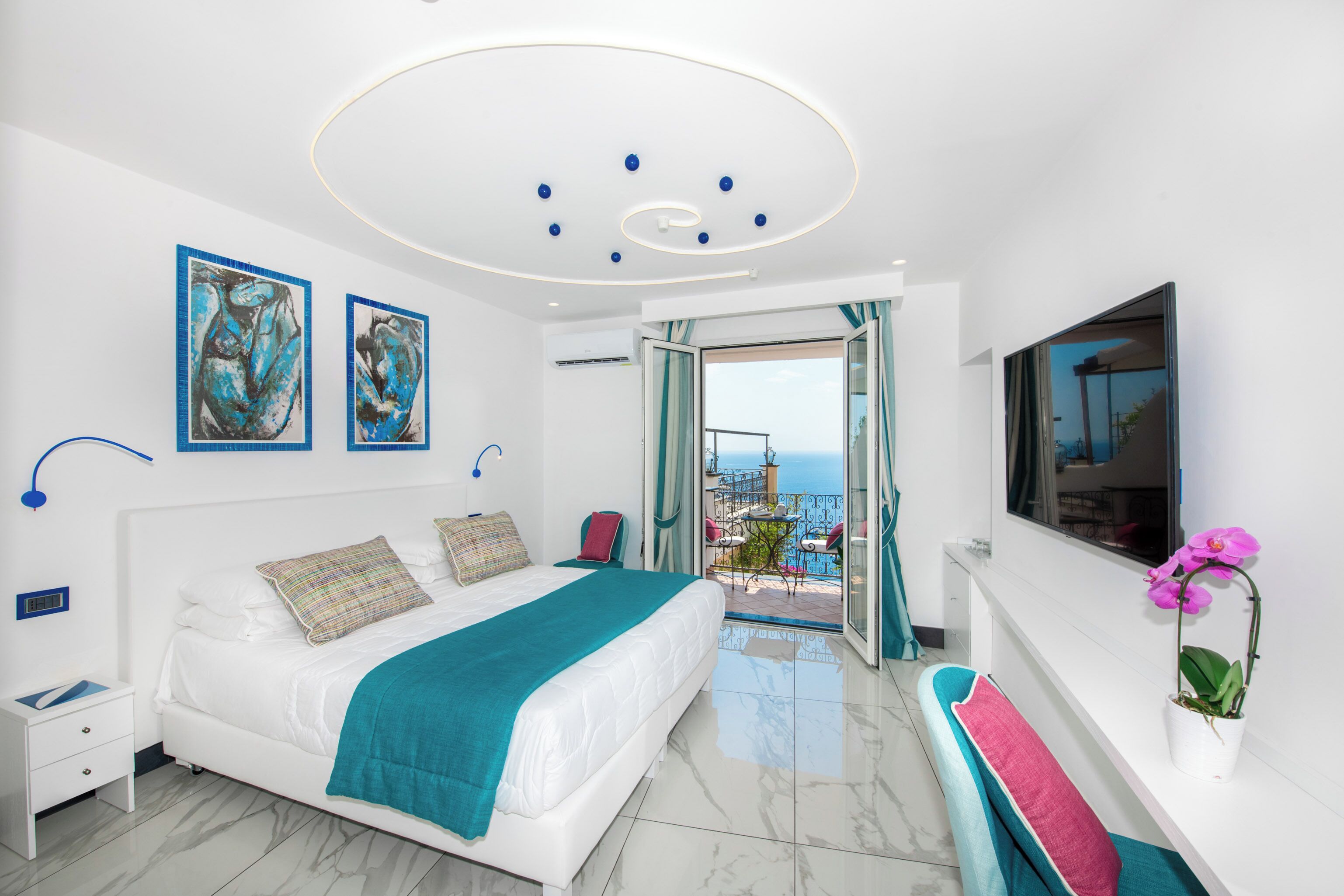 A modern bedroom with a bed, artwork, a TV, and a balcony with a view.