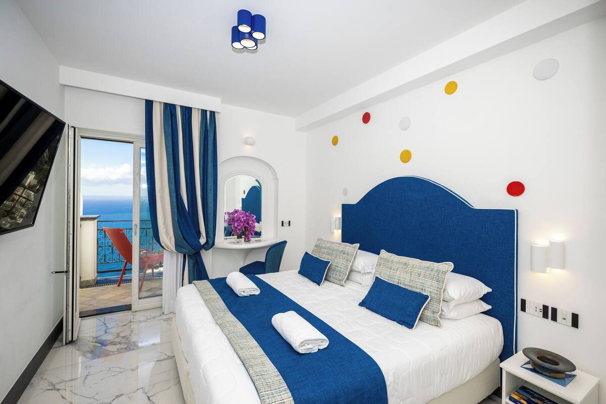 A hotel room with a large bed, a balcony with a view, a TV, and a modern decor.