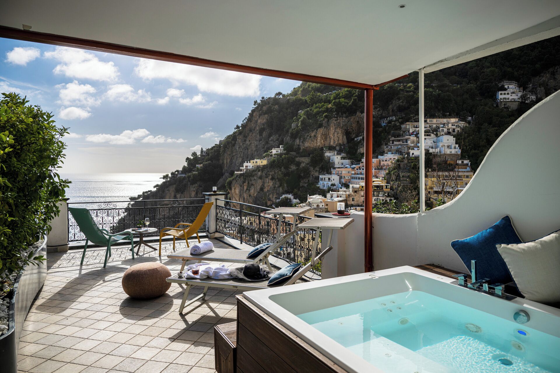 A balcony with a view of the sea, a hot tub, lounge chairs, and a table with a bottle.