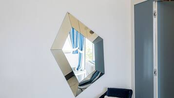 Una habitación moderna con un sofá azul, una silla, un espejo de pared original y una lámpara en el techo.