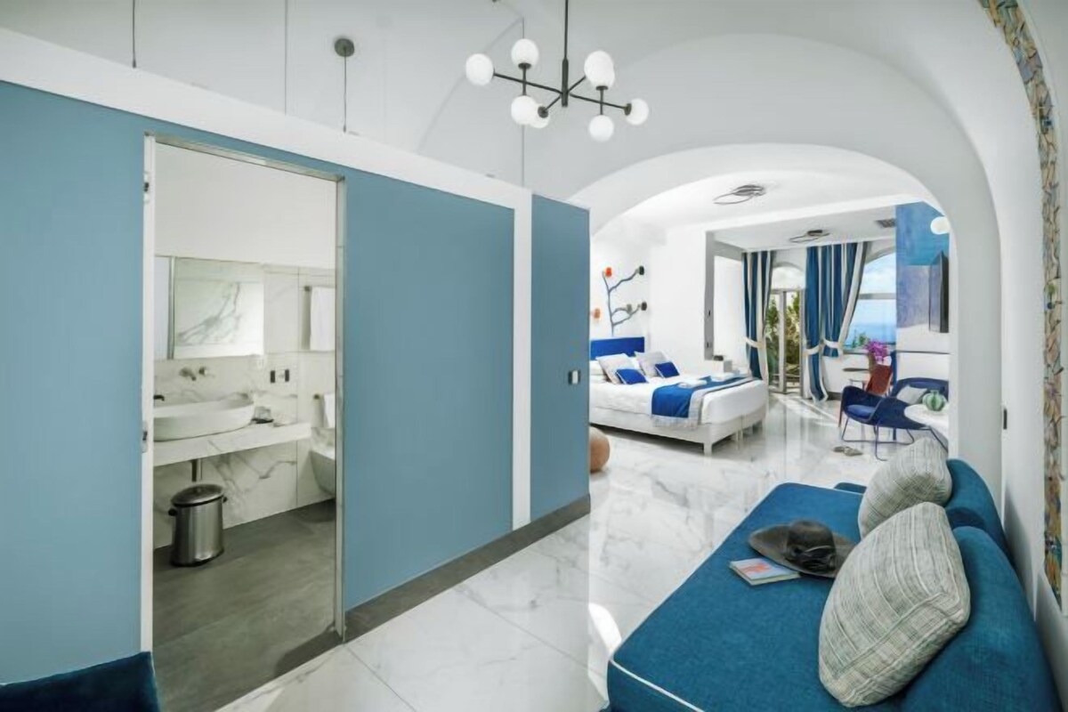 Una habitación moderna con sofá, zona de comedor y baño con espejo y lavamanos.
