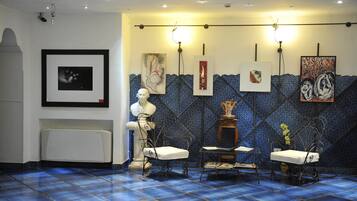 Una habitación con suelo azul estampado, radiador blanco y dos sillas blancas con estructura metálica.