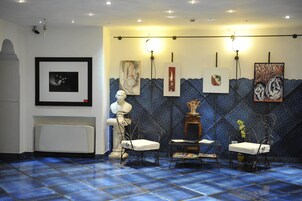 Una habitación con suelo azul estampado, radiador blanco y dos sillas blancas con estructura metálica.