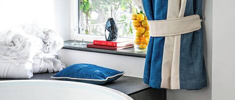 Um banheiro moderno com hidromassagem, degraus revestidos de azulejos escuros, uma janela com cortinas e vista para o verde lá fora.
