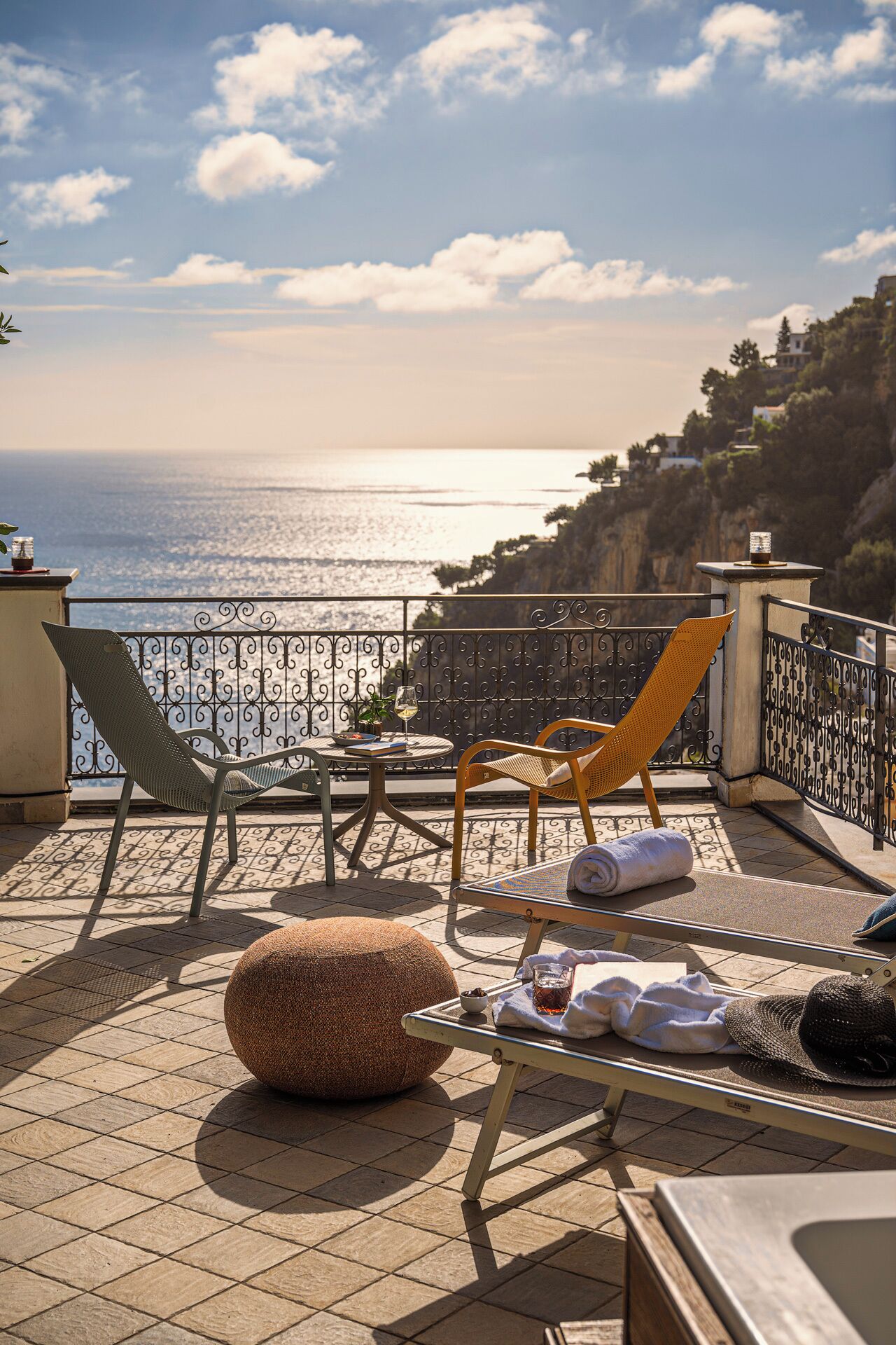 A terrace with two chairs, a round table, a potted plant, and a view of the sea.