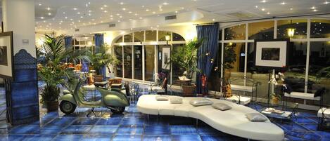 A spacious lobby with a blue-tiled floor, a curved white sofa, and a green scooter.