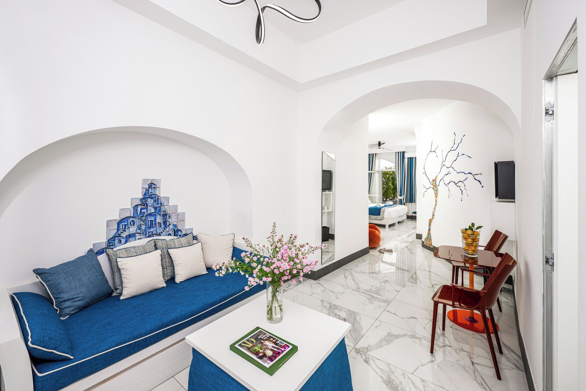 A modern living room with a blue sofa, a white coffee table, and a vase of flowers.