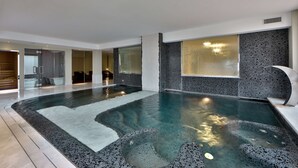 En modern inomhuspool med en vägg som har en yta med småsten och en glasvägg som omsluter poolen.