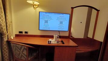 Une chambre d’hôtel équipée d’un bureau, d’une chaise, d’une lampe et d’un écran numérique affichant des informations sur l’hôtel.
