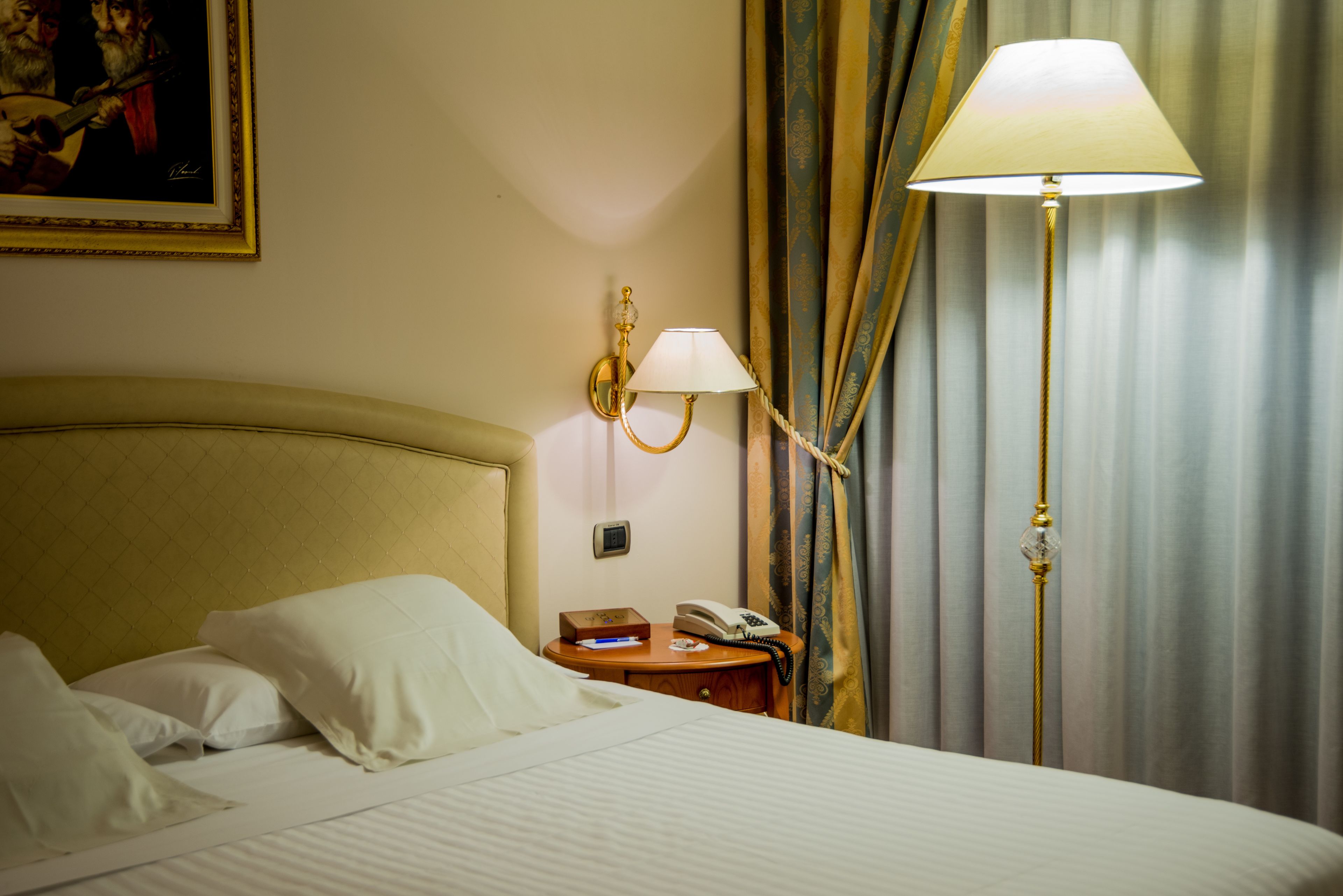 Ein Hotelzimmer mit Bett, Nachttisch mit Lampe, Telefon und einem Gemälde an der Wand.