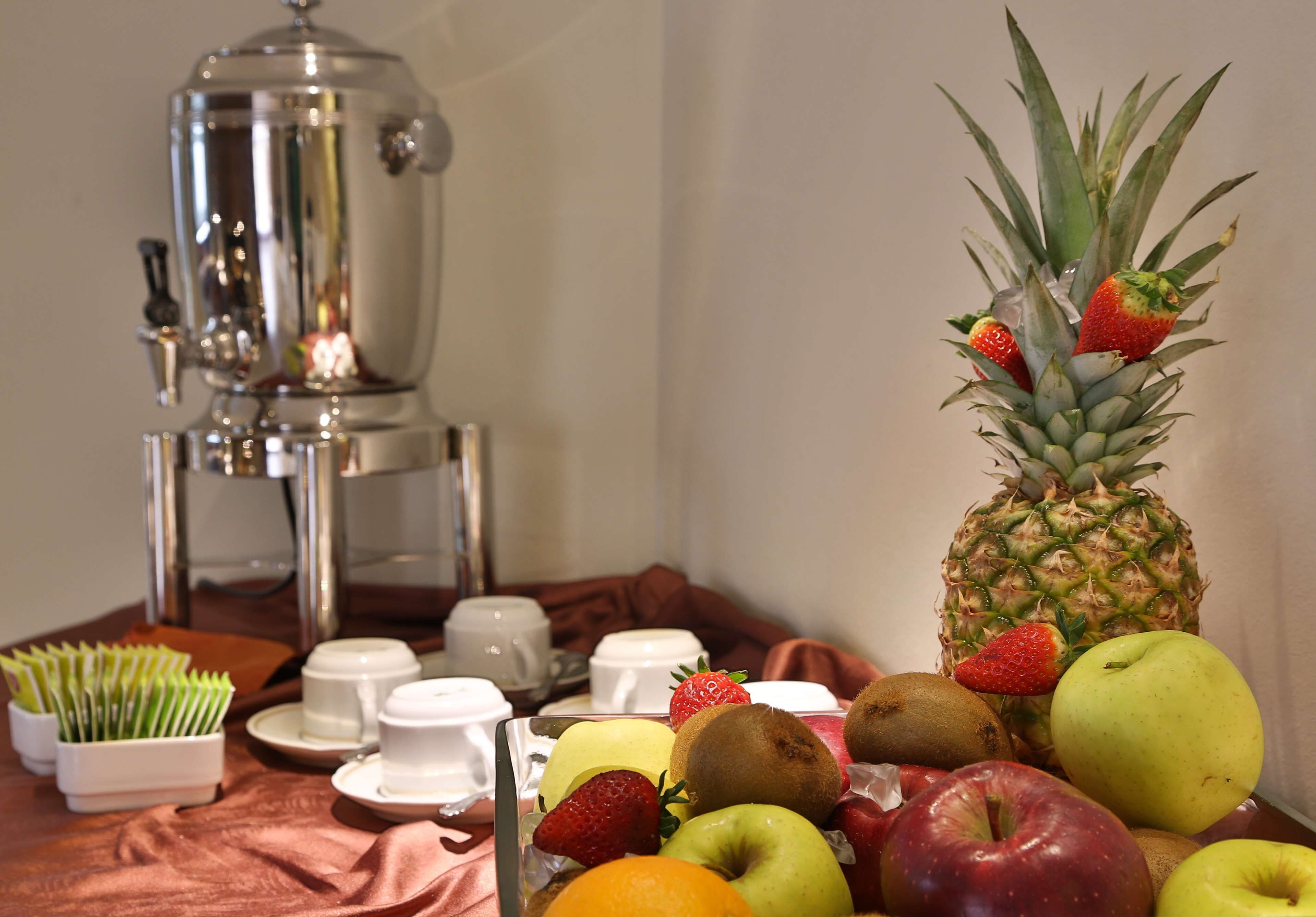 A breakfast buffet with fruits, a coffee maker, and white cups on a table.