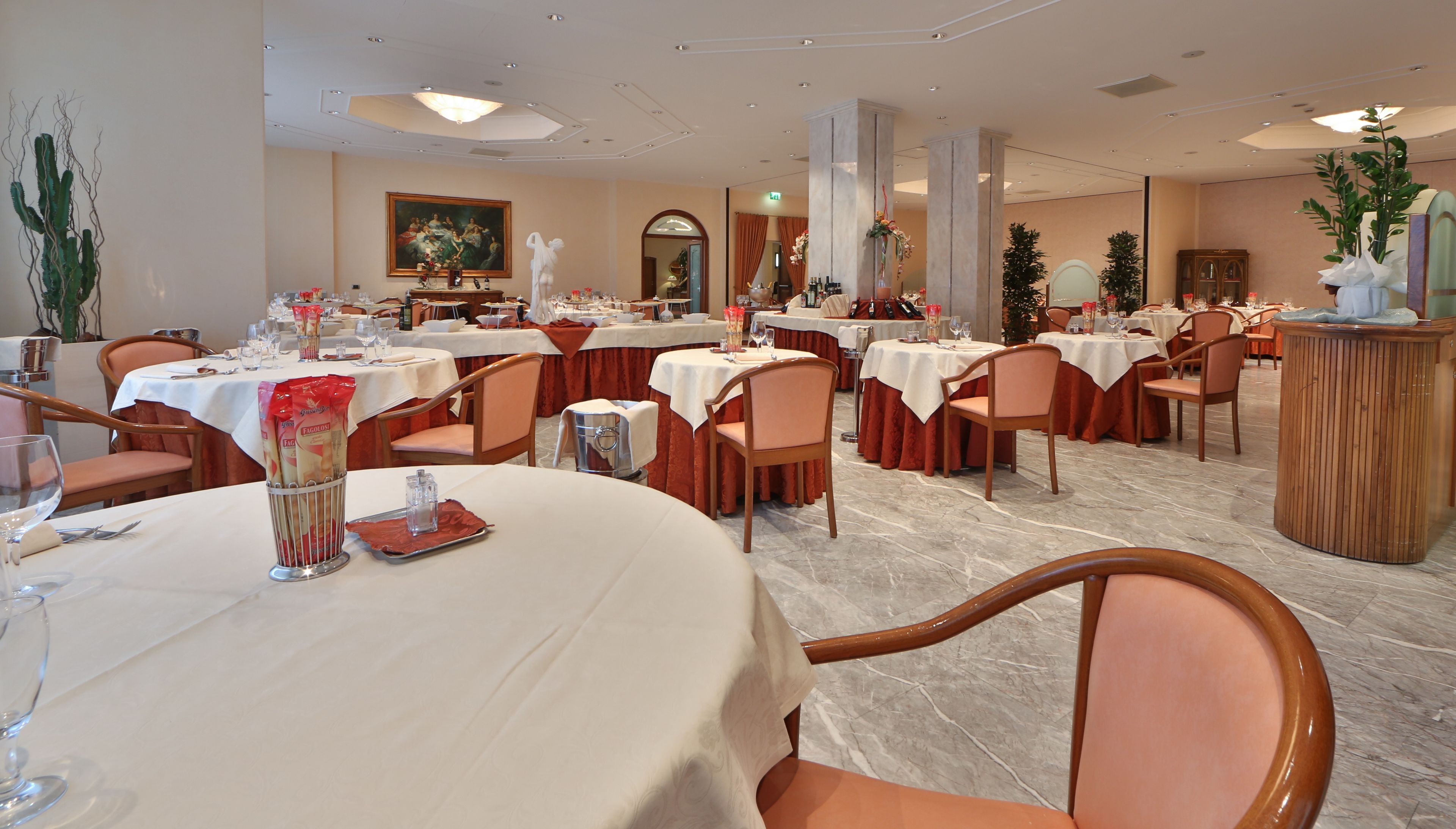 Un comedor formal con varias mesas dispuestas para el servicio, suelo de mármol y un diseño arquitectónico clásico.