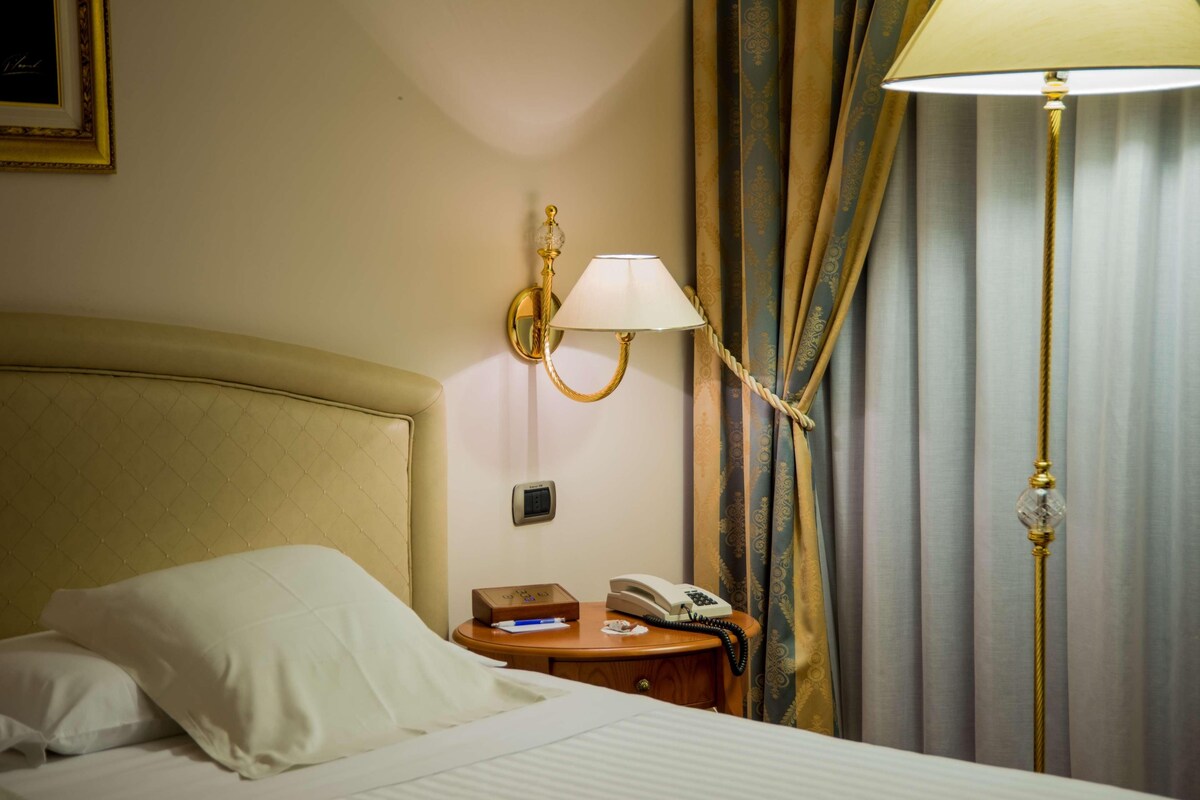 Una habitación de hotel con una cama, una mesita de noche, una lámpara, un teléfono y cortinas.
