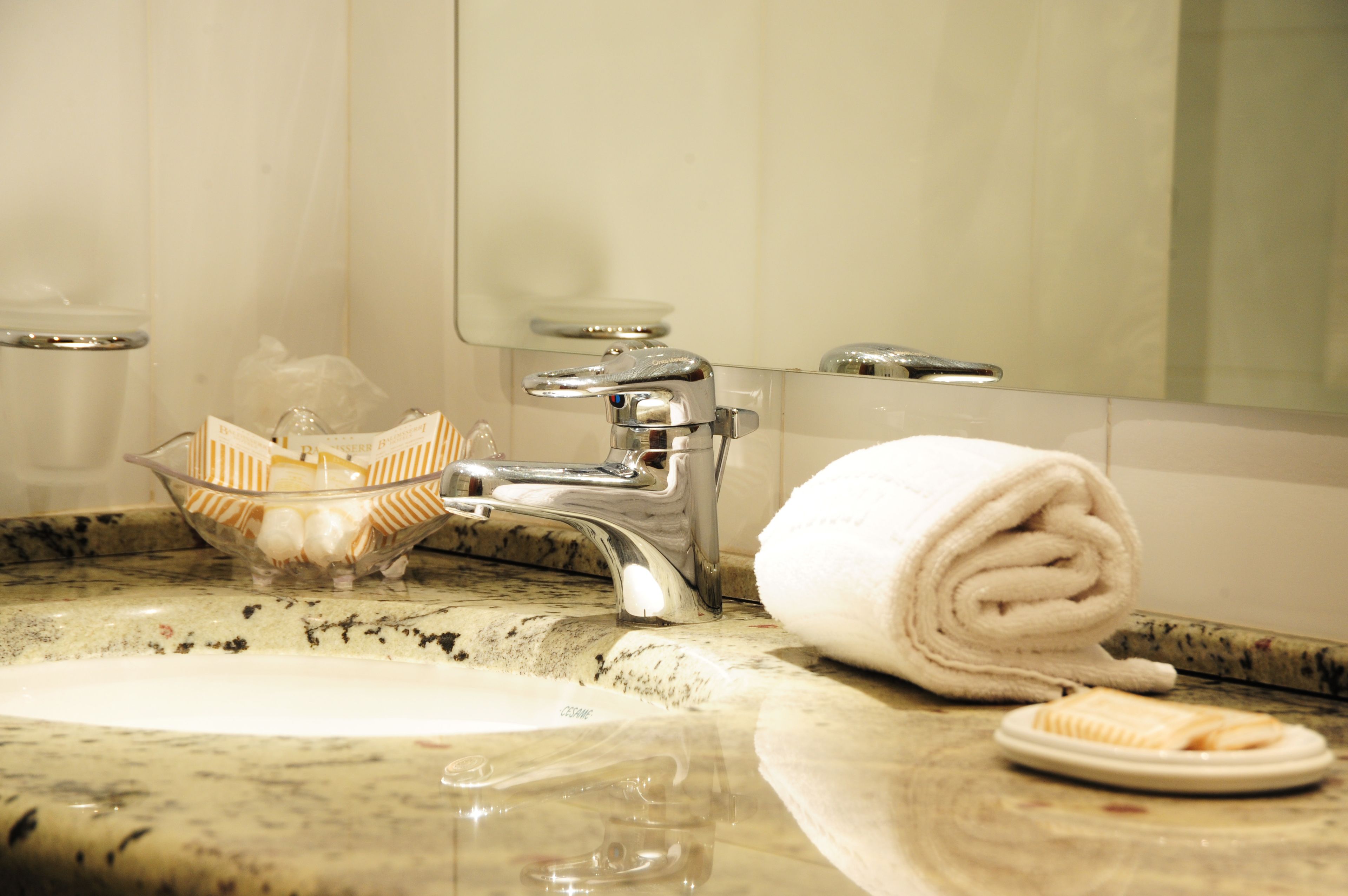 A bathroom sink with a glass bowl containing toiletries, a towel, and a toothbrush.