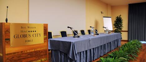 Un salón de conferencias con una mesa larga, micrófonos y un atril con una placa.