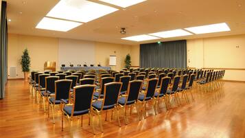 Un salón de conferencias con filas de sillas, un atril y una pantalla para proyector.