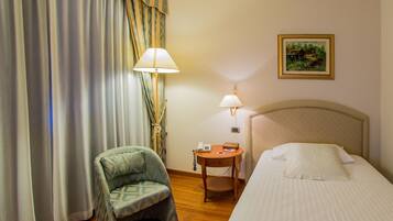 Una habitación de hotel con cama, una silla, una mesita de noche con lámpara y un cuadro en la pared.