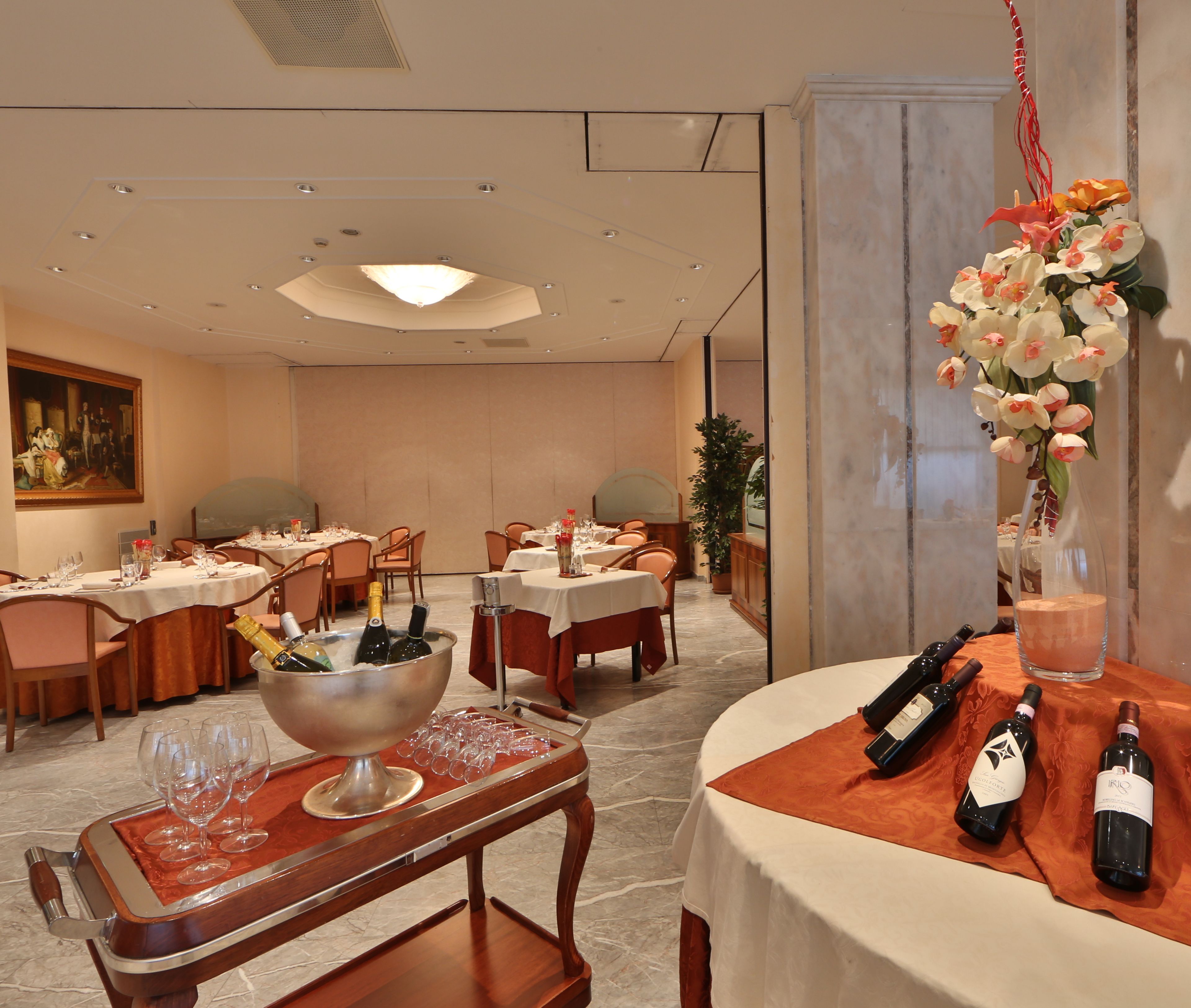 A dining area with tables set for a meal, a bar area with bottles and glasses, and a decorative flower arrangement.