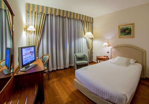 Una habitación de hotel con una cama, un escritorio con una computadora, una silla y cortinas.