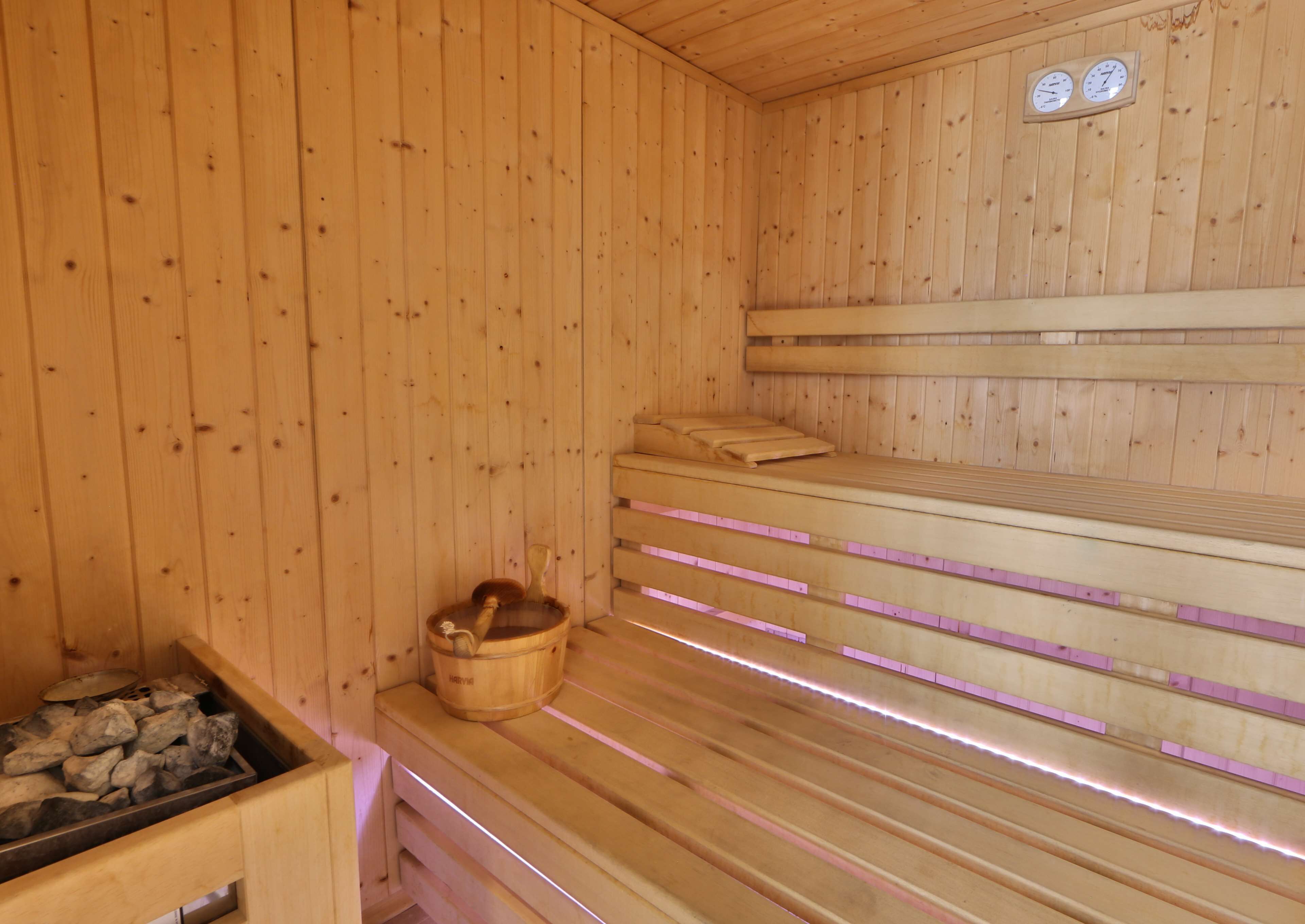 Una sauna de madera con bancos, un cubo de madera y un recipiente lleno de piedras.