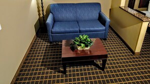 A hotel room with a blue sofa, a small wooden coffee table with a plant, and three framed pictures on the wall. - Comfort Inn Fort Collins North (Fort Collins)