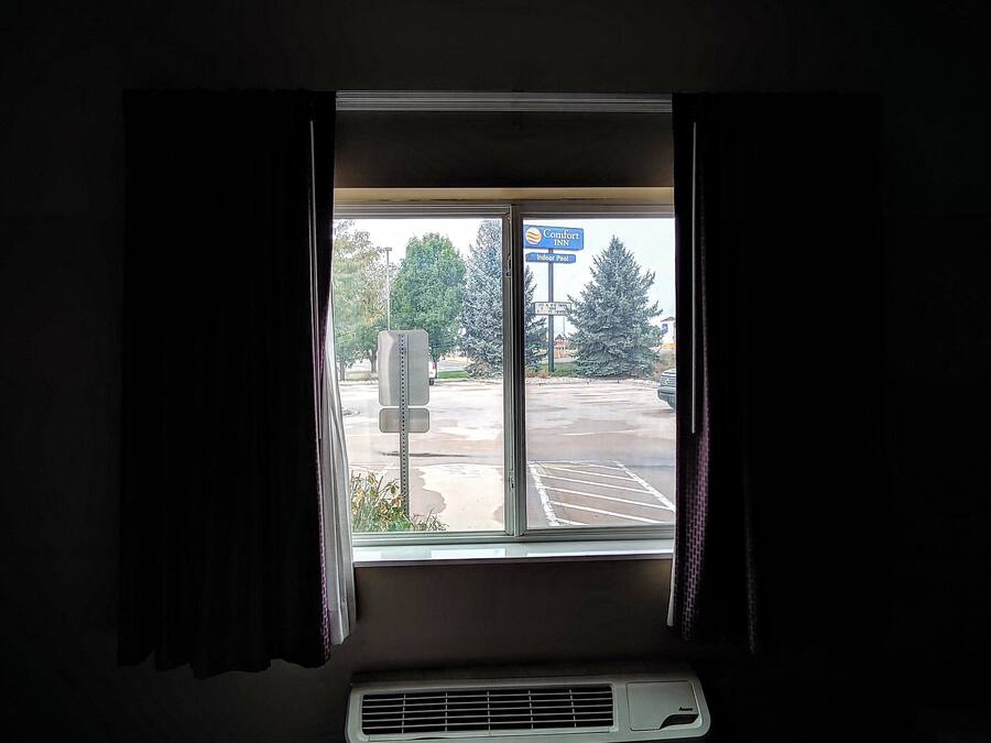 A hotel room with a large window, a bed, and an air conditioning unit.