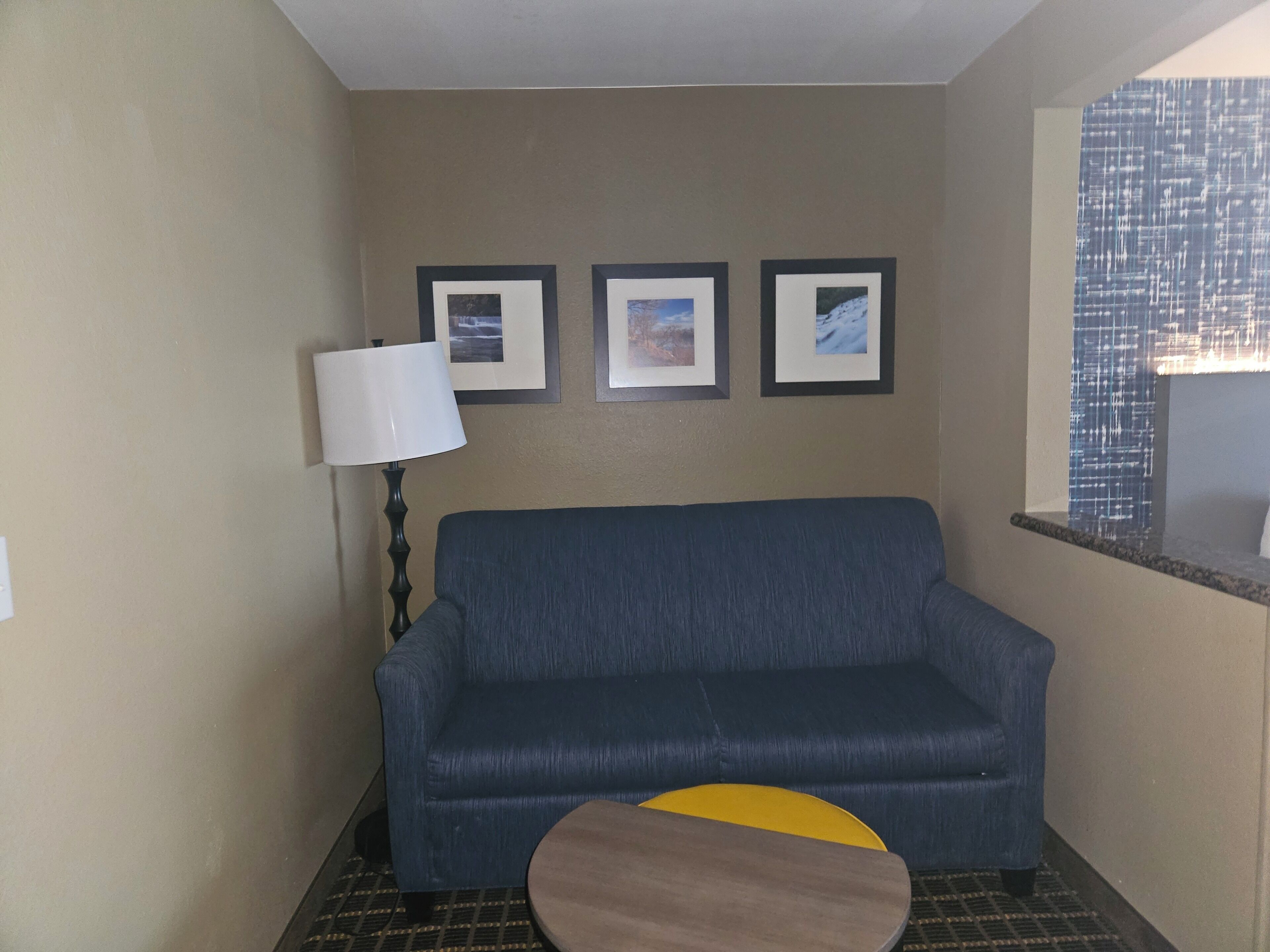 A room with a blue sofa, a small round table, and three framed pictures on the wall.