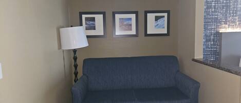 A room with a blue sofa, a small round table, and three framed pictures on the wall.