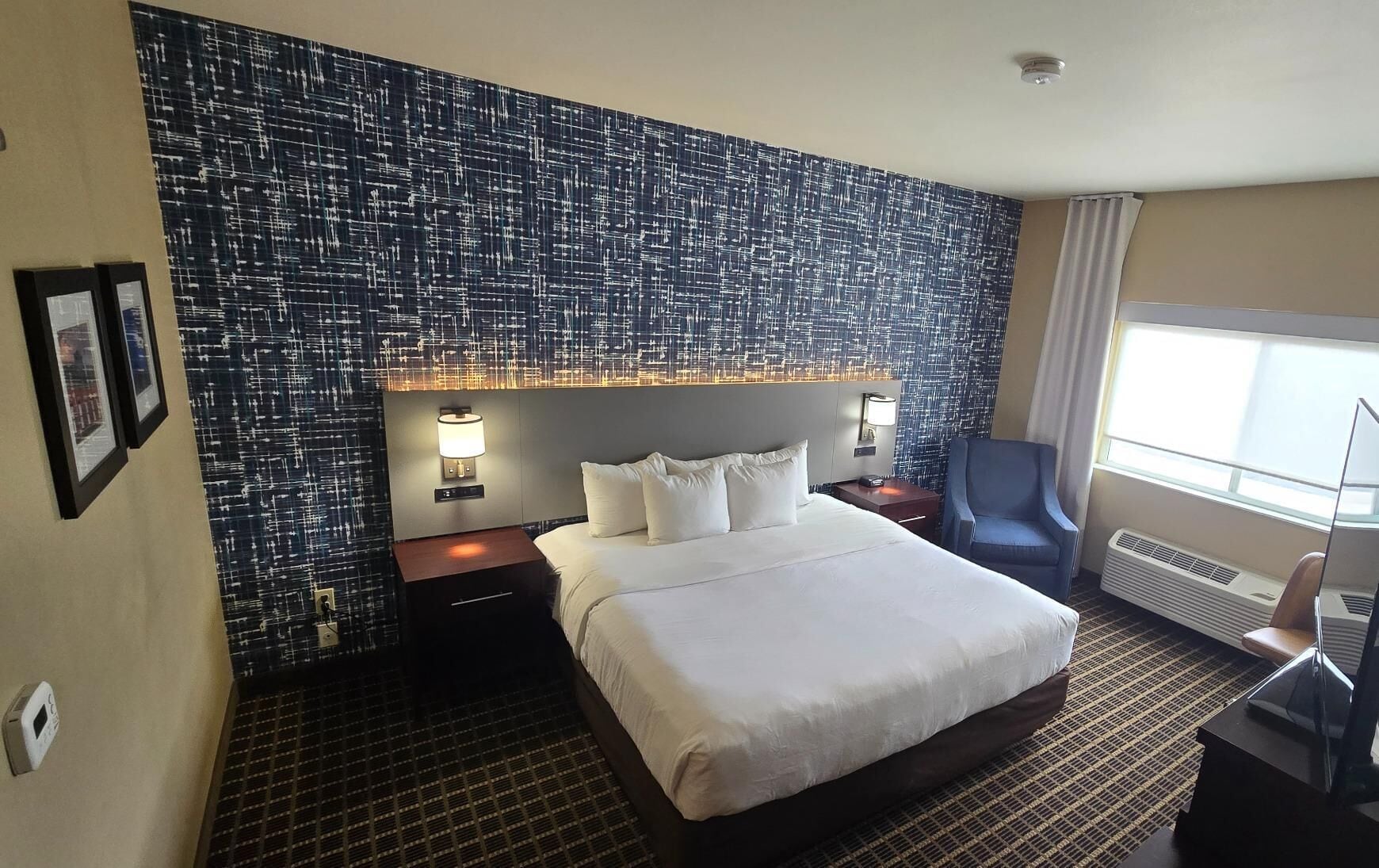 Ein Hotelzimmer mit einem großen Bett, einem Schreibtisch, einem Stuhl und einer Wand mit Muster.