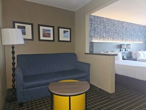 Una habitación de hotel con un sofá azul, una mesita amarilla, una cama y una pared decorada con cuadros.