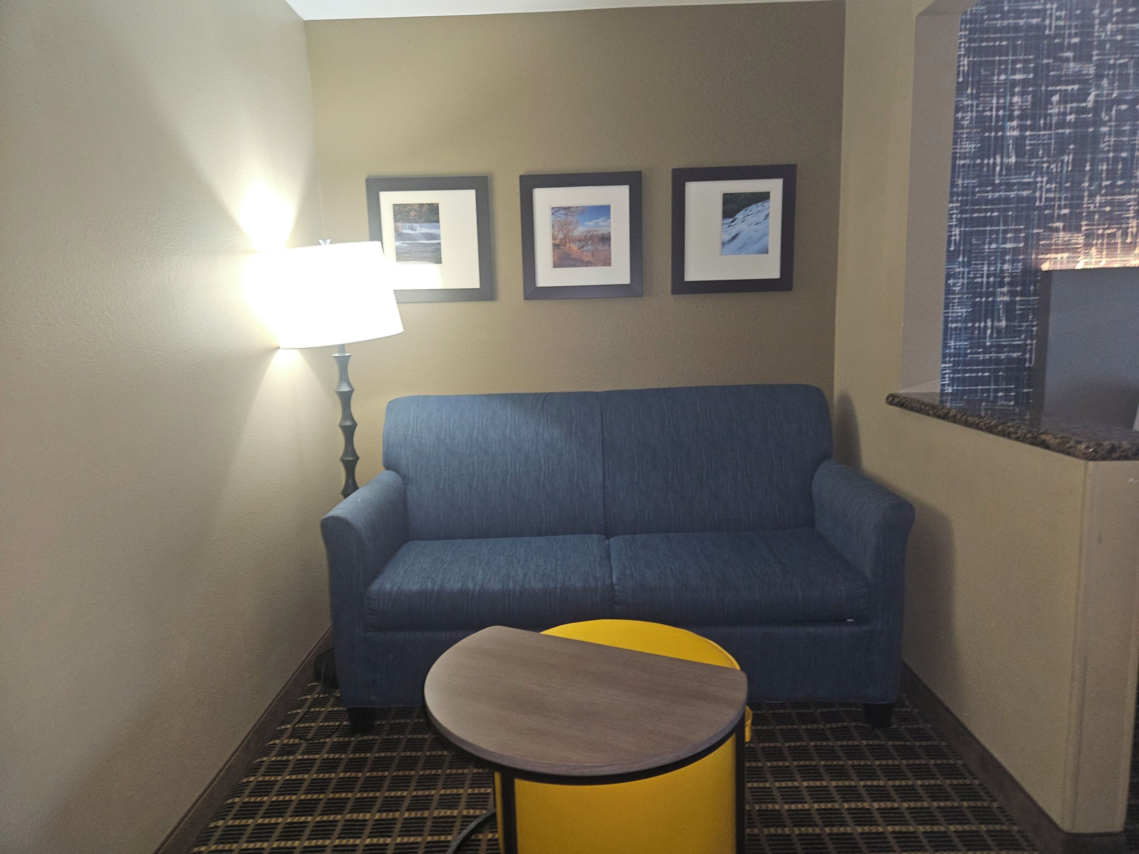 Una habitación con un sofá azul, una mesa redonda pequeña, una lámpara y tres cuadros en la pared.