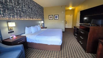 A hotel room with a large bed, a desk with a lamp, a television, and a wall-mounted light fixture.