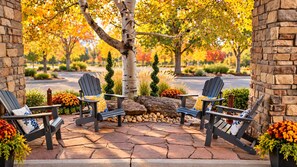 A patio with Adirondack chairs, a stone wall, and a tree with autumn leaves.