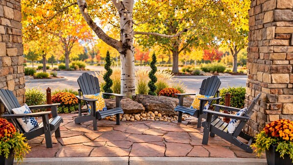 Un patio con sillas Adirondack, un muro de piedra y un árbol con hojas otoñales.