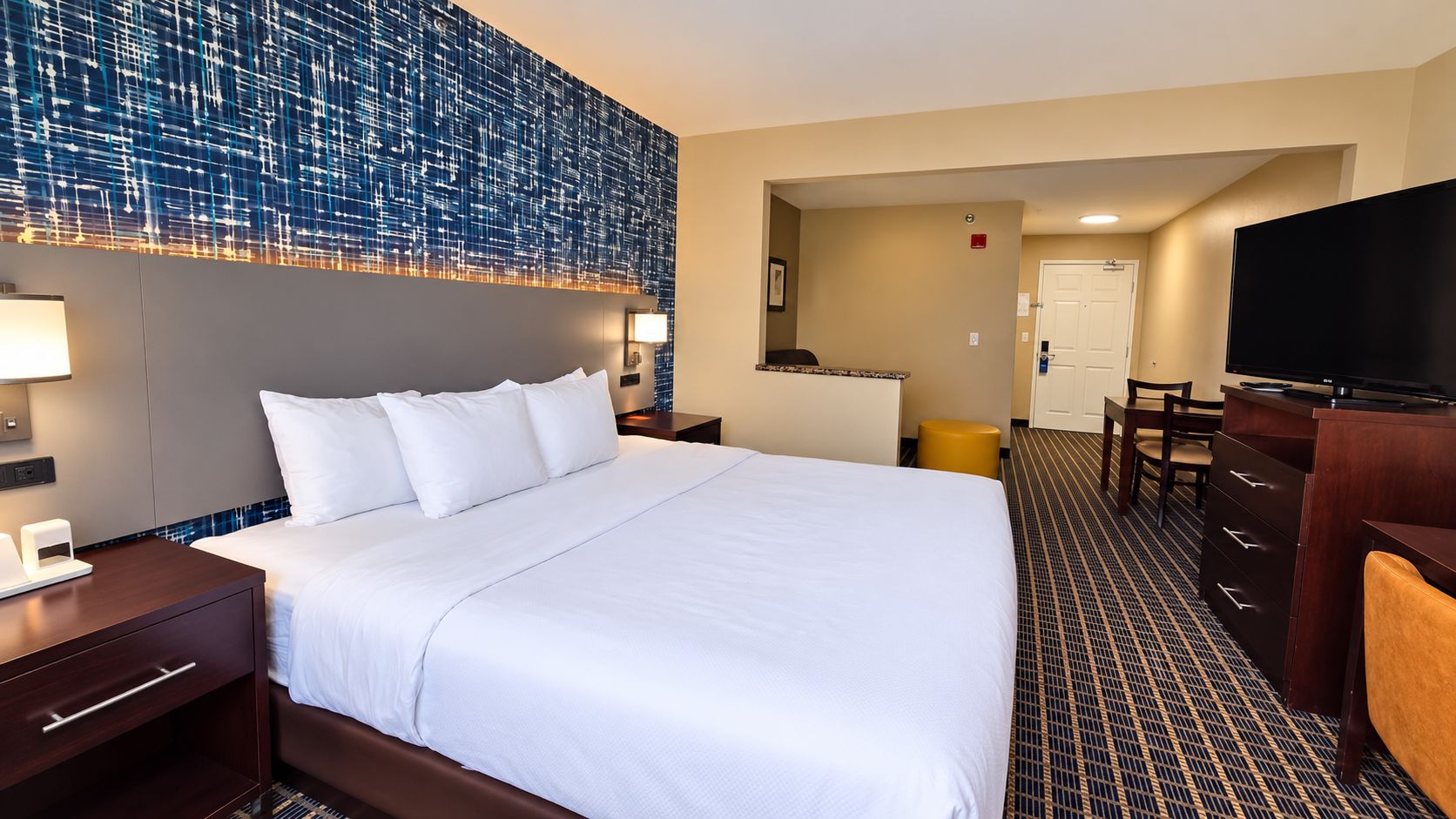 A hotel room with a large bed, a desk with a flat-screen TV, a chair, and a wall-mounted TV.