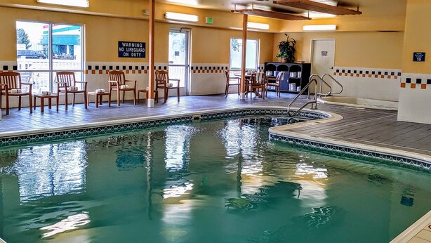 A pool area with chairs and a table, a sign warning no lifeguard on duty, and a view of the outside.