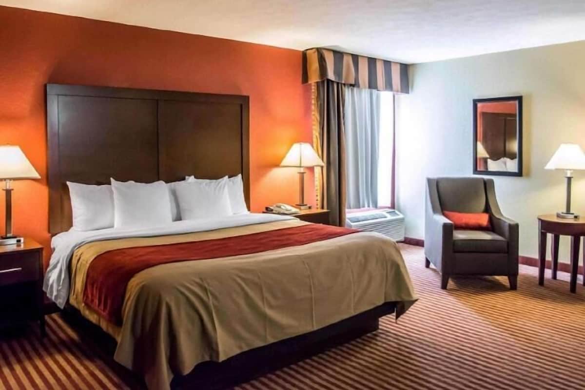 A hotel room with a large bed, two bedside tables with lamps, a chair, and a window with curtains.