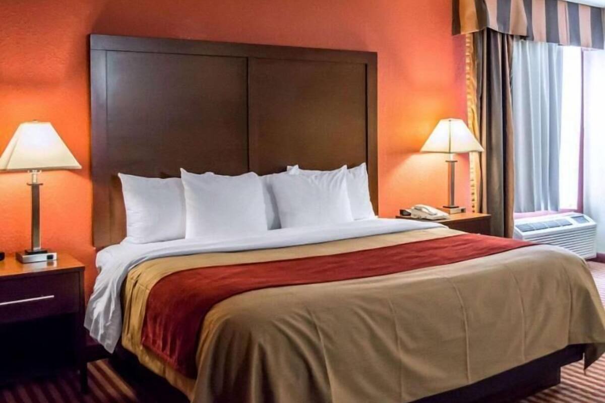 A hotel room with a large bed, two bedside lamps, a telephone, and a window with curtains.